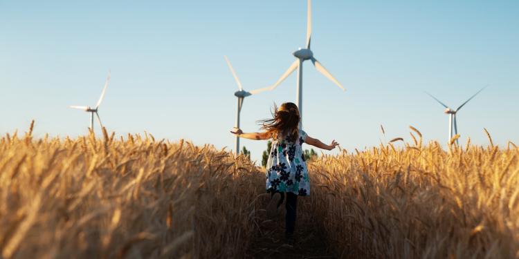 a child runs through a field of wheat with wind turbines in the background